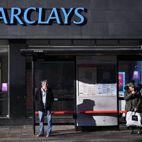 Commuters wait at a bus stop outside a branch of Barclays in London.