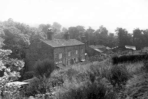 Long shot of stone built cottages on Scotland Mill Lane in September 1959. On the left are numbers 6 to 3 with numbers 2 and 1 seen towards the right, lower with protruding outbuildings. The cottages were originally built to house Scotland Millworkers. The mill itself burnt down in 1906.