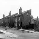 Raby Mount, seen from Sheepscar Street. Just seen on the left edge is the wall of a new Police Section House. At the end of Raby Mount, premises belonging to G.W. Binns, motor garages are visible. Raby Mount at this point comprised 3 pairs of houses. On the right is Yeomanry Street. Pictured in May 1958