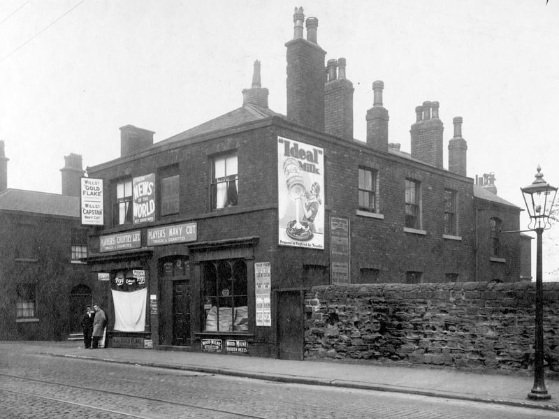 Low Road in September 1929 On left, junction with Highgate Street. Next, number 7 John Normington newsagent. Various advertising signs can be seen, including Wills Tobacco, Players tobacco, 'News of the World' sunday newspaper. The shop window is covered by a blind. Two men stand in the doorway. Number 9 John Benson Hardaker, boot repairs. Goods in this window are covered by a sheet of paper.