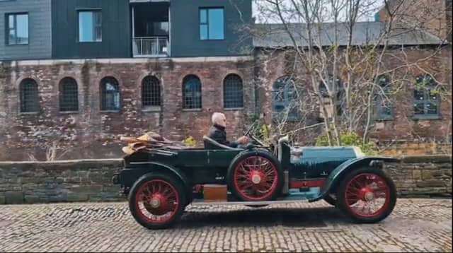 An antique car driving down a cobbled street