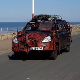 A zombie themed vehicle driving on a road by the coast