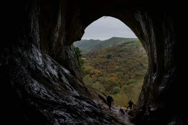 Walkers enter Thor's Cave, framing the Autumn colours in the valley below. Thor's Cave is a natural limestone cave formation in the Manifold Valley in the Staffordshire Moorland area of the Peak District.