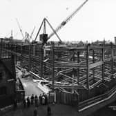 A crowd of onlookers stand at the junction of Wade Lane with Mark Lane, watching the progress being made on the new Lewis's store on The Headrow in November 1931.