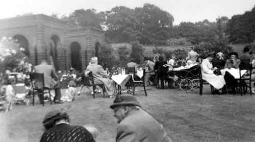 .eople seated at tables enjoying a summer garden party in the walled garden of Lotherton Hall in the late 1940s or early 1950s.