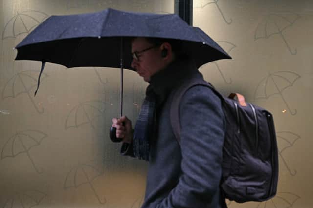 A commuter shelters from the rain under an umbrella in January 2025.