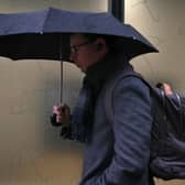 A commuter shelters from the rain under an umbrella in January 2025.