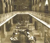 Looking from the gallery down to the Reference Library on the second floor of Leeds Central Library. This room is on the south side of the building and fronts onto The Headrow. Many people are seated at the long desks studying or reading.