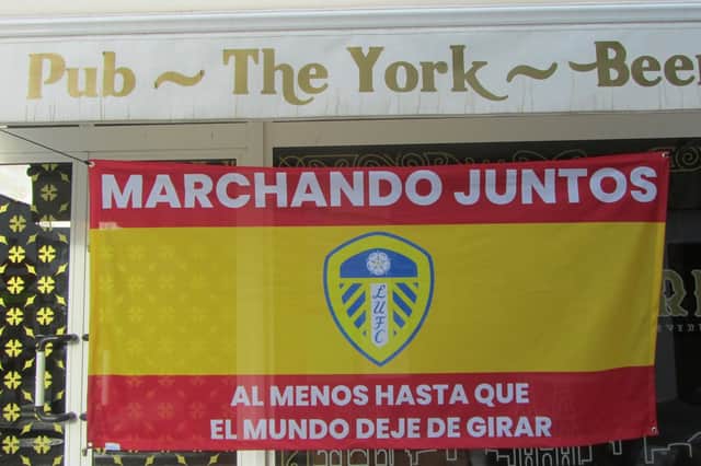 The flag reads 'Marching On Together' and then 'at least until the world stops going round' in Spanish.