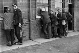 Miners are pictured circa 1950s collecting their wage tally from the first window, allowing them to draw their wages from the second window.
