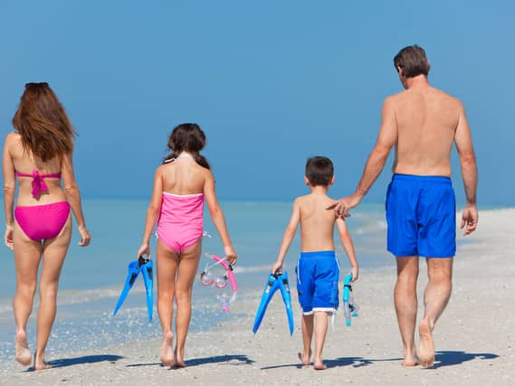 A happy family of mother, father and child, a daughter, walking in swimming costumes on a sunny beach