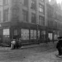 The junction of New Market Street with Kirkgate former premises of Tiger Stores. Statue of tiger sited above doorway. Women, men and children in period dress pose on corners of roadside. Pictured in July 1907.