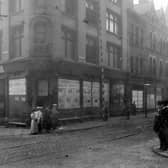 The junction of New Market Street with Kirkgate former premises of Tiger Stores. Statue of tiger sited above doorway. Women, men and children in period dress pose on corners of roadside. Pictured in July 1907.