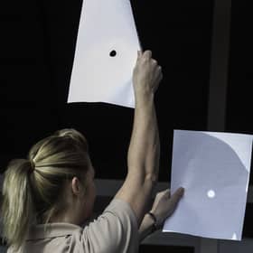 A woman uses two sheets of paper as the Sun is obscured by the Moon during a partial solar eclipse at Skegness seafront in Lincolnshire, north England on 20 March 2015.