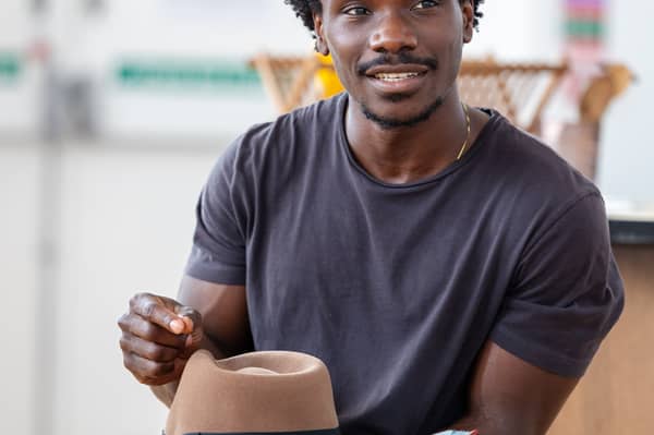 Josh Tedeku as Cory Maxson, holding a script and a fedora.