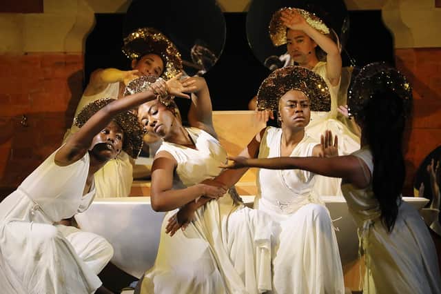 Dancers adorned in white draped tunics and textured gold halo headpieces strike dramatic postures in an ensemble scene from Ecstasy of the Virtues