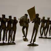 A collection of detailed bronze sculptures by Betty Miller depicting a marching brass band, featuring horn players, a bass drummer, and a flag bearer