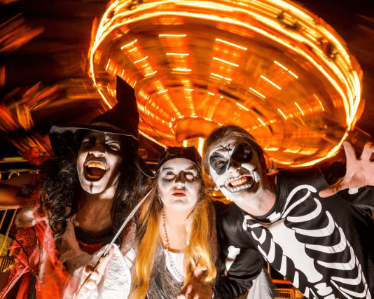 Spooky costumed characters strike a pose in front of a spinning fairground ride during Lightwater Valley's Frightwater Valley Halloween event