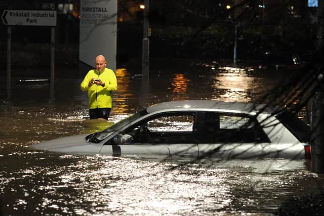 A pedestrian wades through floodwater on Kirkstall Road Leeds past an abandoned car after the River Aire burst its banks. Photo credit: Tony Johnson