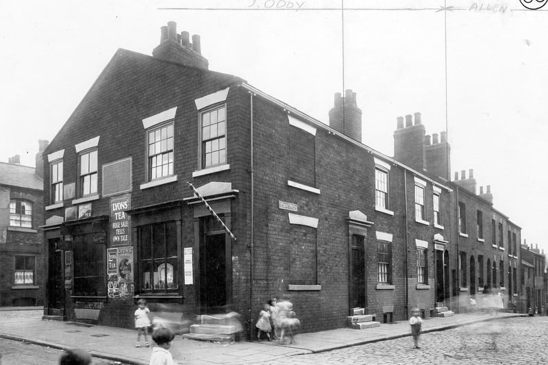 The corner of Acorn Street and Great Garden Street, showing back-to-back terraced houses, children in street, and corner shop with striped barbers pole and poster for Lyons Tea.