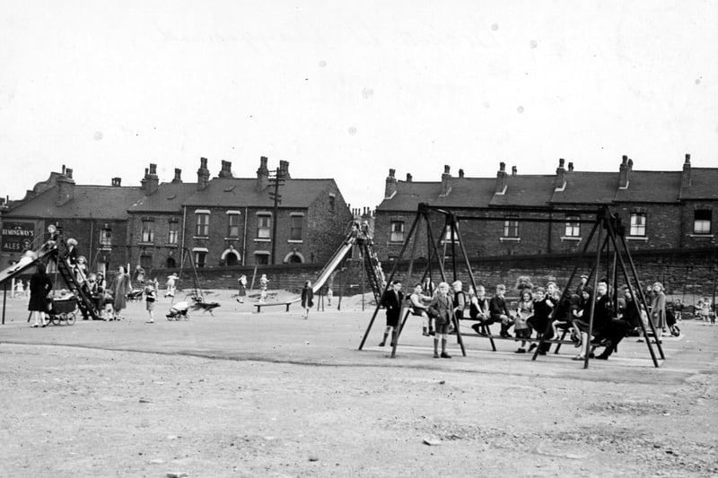A view shows children playing on swings and slides in Beckett Street recreation ground. The terraces of red brick houses in the background are in Arthur Street.