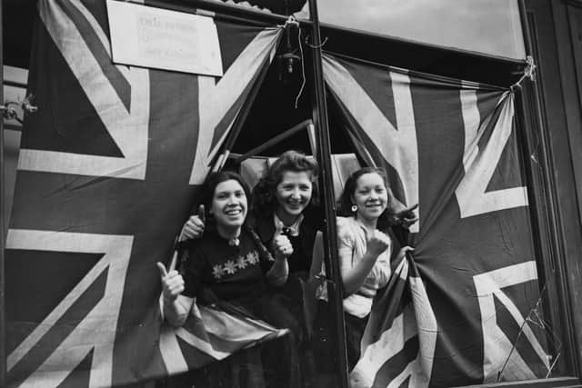 Three young women giving the thumbs-up through union jack flags, used to cover the broken windows of a cycle painting shop in south London, after an air raid in September 1940. (Getty Images).