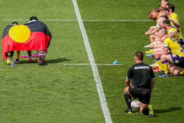 Wigan's Bevan French and Trinity's Dave Fifita display an aboriginal flag as Warriors players take a knee. Picture by Alex Whitehead/SWpix.com.
