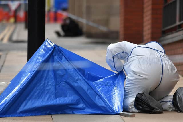 A police forensics officer looks under a small blue police tent covering an area of pavement in Livery Street. PIC: PA