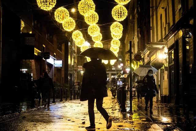 A man holding an umbrella crosses a quiet street filled with Christmas lights in Westminster, London, at the start of the first full week of the four week national lockdown in England.