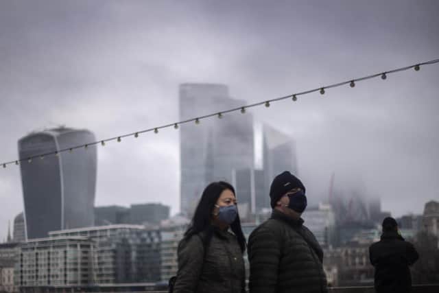 File photo of a couple wearing face masks walking past a view of the City of London.