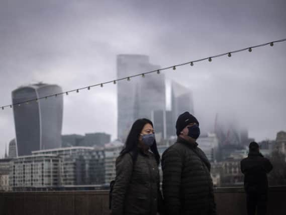 File photo  of a couple wearing face masks walking past a view of the City of London.