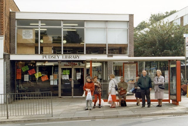 Pudsey Branch Library on Church Lane which was built in 1963 and opened on the in January 1964. Various notices are displayed in the windows. A queue of people are waiting at a bus shelter in front.