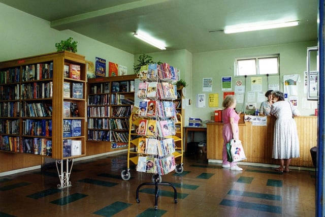 Inside Cow Close Branch Library, situated on Whincover Drive. Bookshelves are on the left with a paperback stand in the centre and the counter on the right.