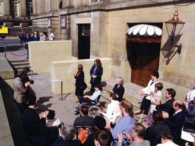 A crowd is gathered outside the Municipal Buildings on The Headrow for the opening of the new ramp providing level access to the Central Library and City Museum in May 1993. The entrance to Stumps public house, also benefitting from the ramp, can be seen on the right, with Calverley Street visible on the left.