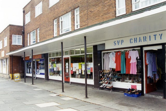 Heights Drive in Armley. Pictured is the SVP Charity Shop with clothes and shoes displayed outside. Next to this is Armley Heights Library, one of Leeds City Libraries' small branches, then at Dewhirsts Newsagents and Post Office.