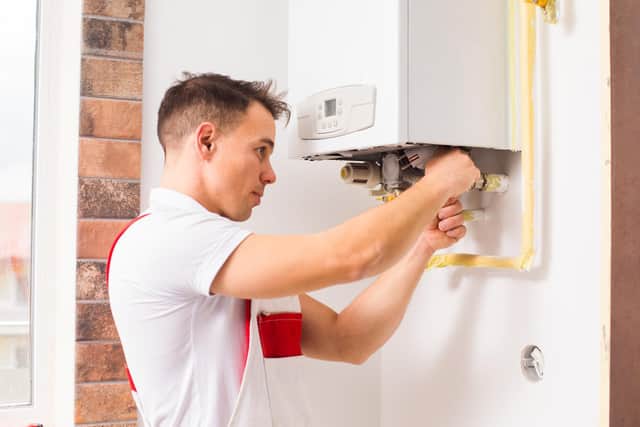 A qualified plumber repairs a boiler. Photo: Adobe