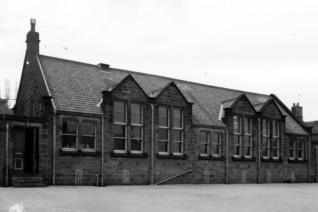 Rodley County Primary School on Town Street in March 1965. The playground can be seen in the foreground while cricket wickets are painted on the school walls below the window. Children peer out of the window to the left.