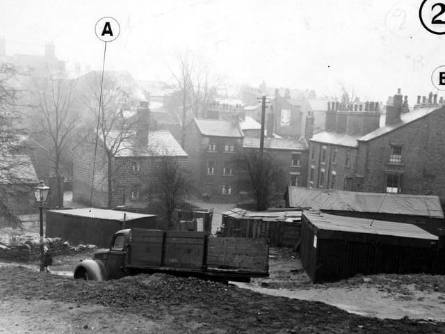 Burley village, with garages and outhouses in the foreground in January 1950. A lorry is parked near one of the garages and a small child is standing next to a lamp post.