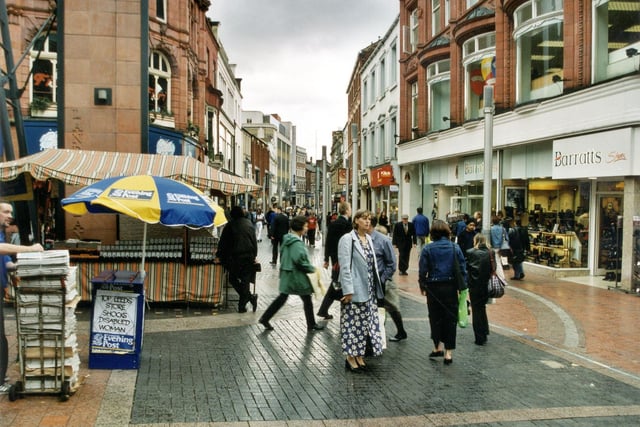 The junction of Lands Lane and Commercial Street in September 1999. There is an Evening Post Newpaper seller on the left with a Watch Stall just behind. On the right is Barratts shoe shop and Klick photo processing next door.