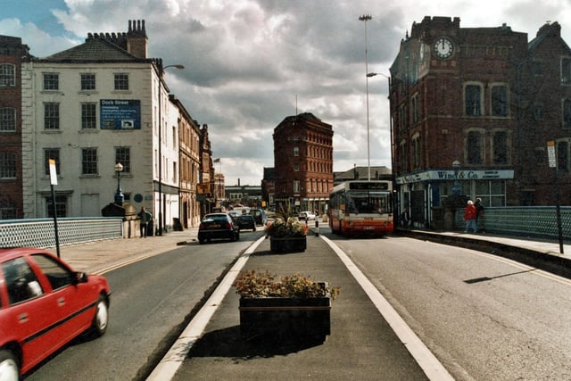 A view on Leeds Bridge in September 1999. Boxed flowers are in place on the island down the middle of the picture. To the left, a poster advertises the impending regeneration work to Dock Street. Junctions to Meadow Lane and Let Road at the bottom of the road. Premises of Wine & Co, charted accountants to the right.