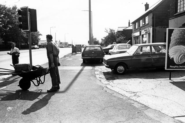 Dewsbury Road at the junction with Old Lane (foreground) in June 1980.  A workman with a wheelbarrow of tools is seen and work on the road is in progress.