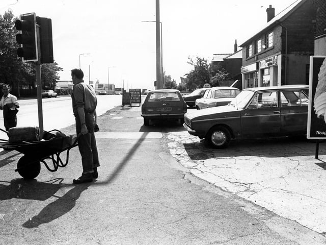 Dewsbury Road at the junction with Old Lane, foreground, in June 1980.  A workman with a wheelbarrow of tools is seen and work on the road is in progress.
