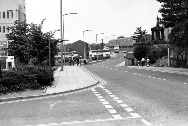 Lower Town Street, with the entrance road to Bramley Shopping Centre in the foreground. On the right the church spire of the old St.Margaret's church can be seen behind a high wall.