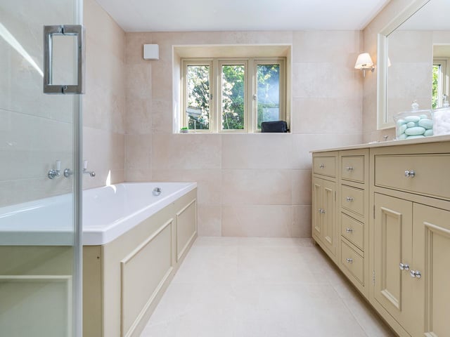 The stylish house bathroom includes both bath and shower, with twin wash basins set within an extended vanity unit.