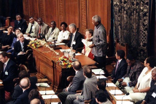 Inside the Council Chamber of the Civic Hall where Nelson Mandela, the former South African President, has risen to make a speech. Seated to his left is the Lord Mayor of Leeds, Coun Bernard Atha and beside the Lord Mayor is the chief executive of Leeds City Council, Paul Rogerson. The lady in cream on the right is the Lady Mayoress of Leeds, Susan Pitter, who for many years helped organise Leeds West Indian Carnival.