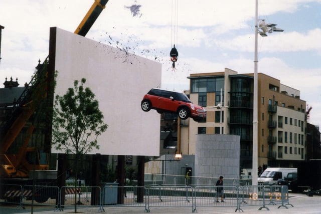 The construction in progress of the BBC Big Screen in Millennium Square in July 2001. A car is being suspended in front of it by a crane. In the background, right, are the recently built luxury apartments of Portland Place on Calverley Street.