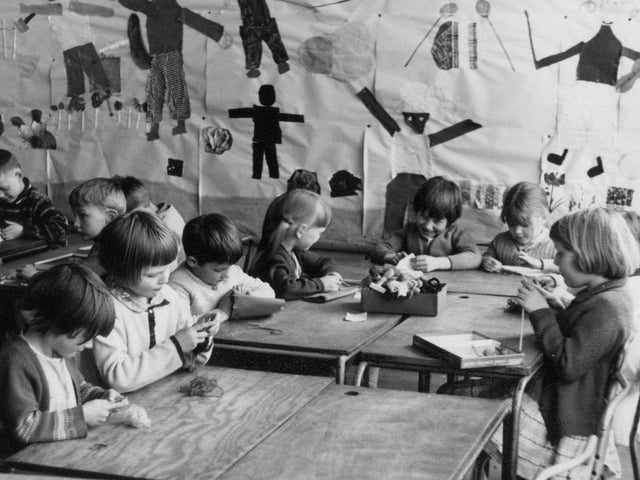 A group of children taking part in crafts activities, including knitting, sewing, and jigsaws. On the back wall is a collage showing a variety of figures.