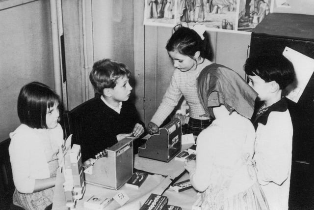 Children at engaged in an activity involving a pretend shop, with cash registers. on 'sale' are sweets and chocolate bars priced at 5d and 1d (old pence). This would have helped them develop numerical skills.