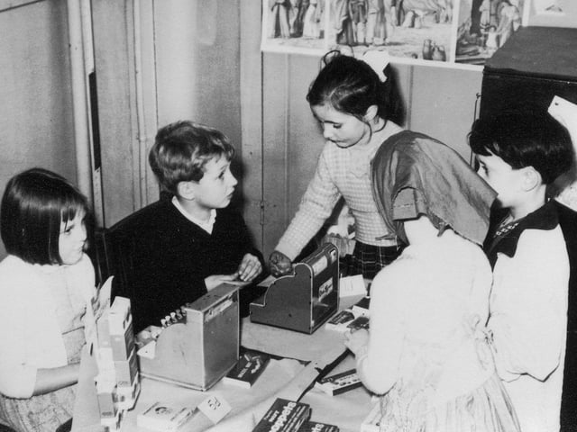 Children at engaged in an activity involving a pretend shop, with cash registers. on 'sale' are sweets and chocolate bars priced at 5d and 1d (old pence). This would have helped them develop numerical skills.