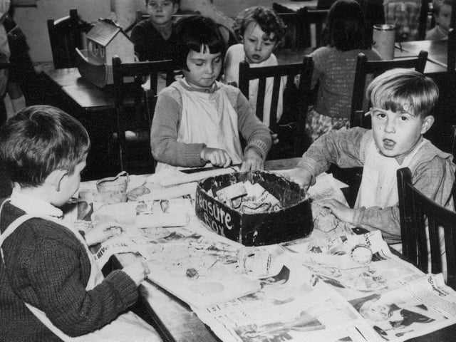 Three children are pictured taking part in a papier-mâché activity, mixing strips of wet newspaper with glue, to create shapes which then harden when dry. In the background, three children are playing with a model of Noah's Ark.